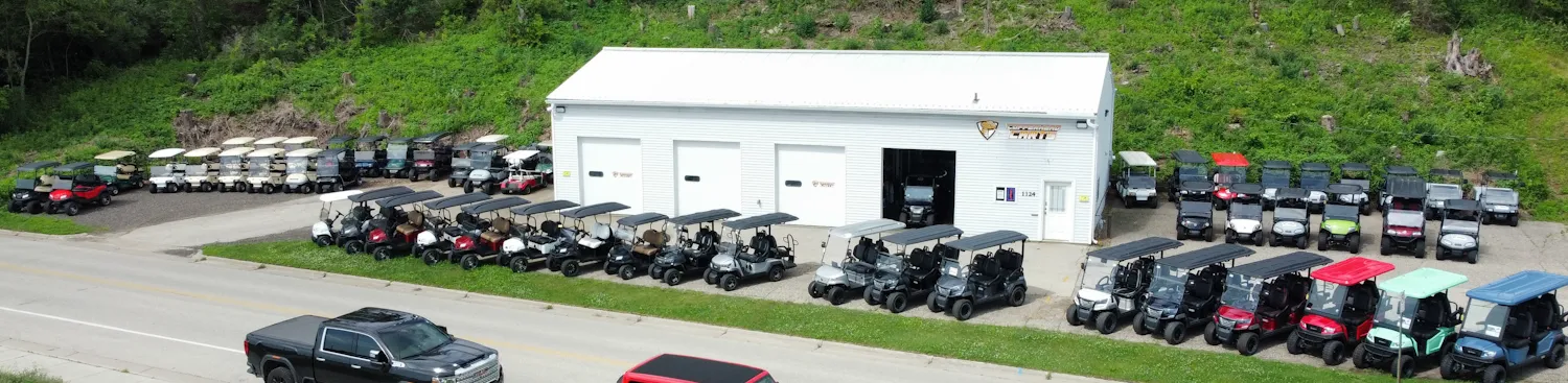 An aerial view of a golf cart dealership with various carts parked outside a white building.